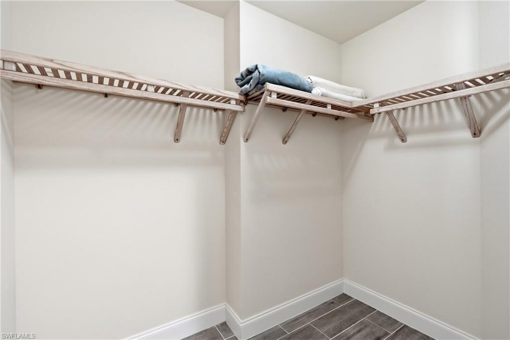Walk-in closet with L-shaped wood shelving, light neutral wall paint, white baseboards, and wood-finish tile flooring