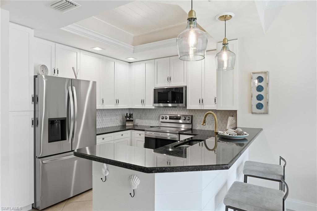 Kitchen featuring stainless steel appliances, white cabinetry, dark stone countertops, and a tile backsplash