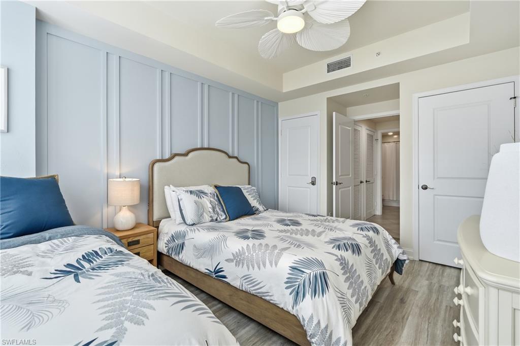 Bedroom featuring a light blue accent wall with vertical paneling, light wood-finish flooring, and a ceiling fan with integrated lighting