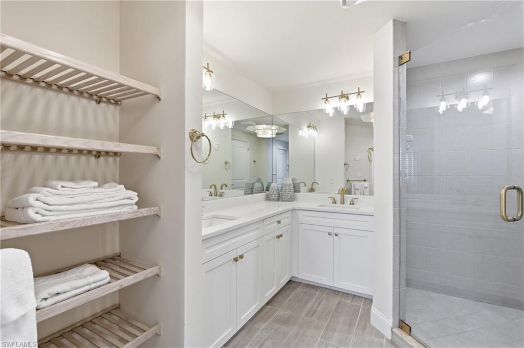 Contemporary bathroom featuring a spacious glass-enclosed shower with large format tile, dual vanity with white cabinetry and integrated sinks, and ample built-in shelving