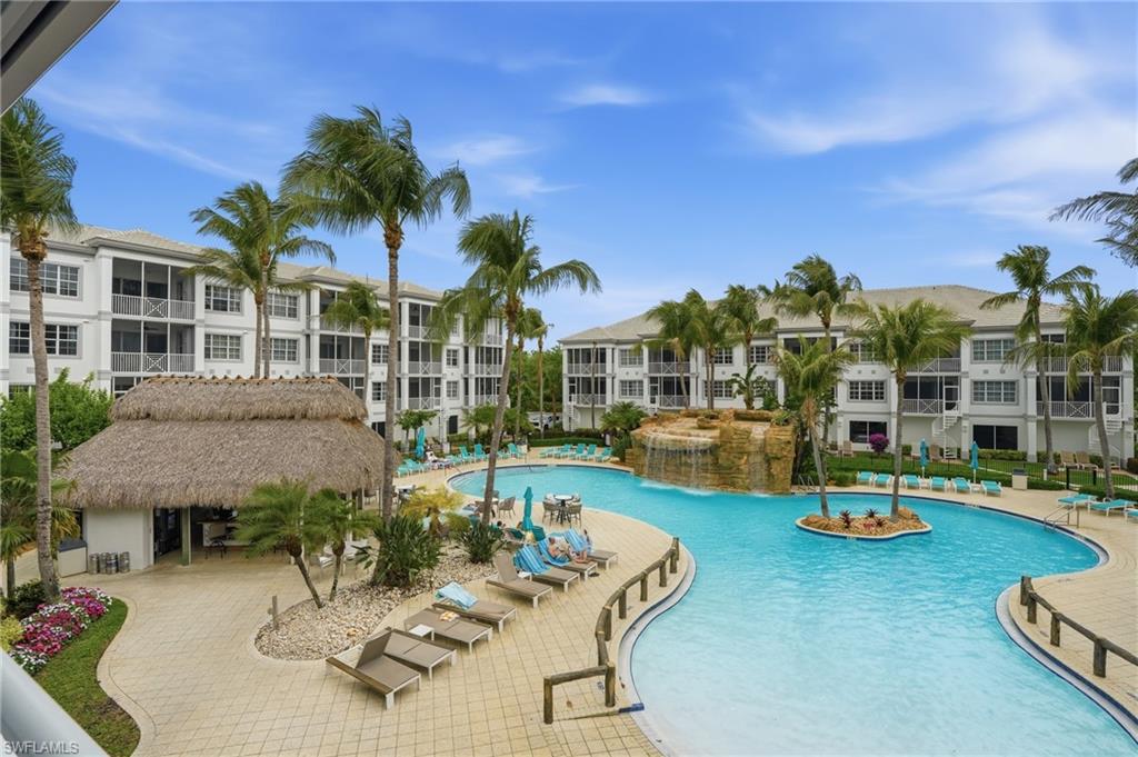 Expansive resort-style pool area featuring a winding swimming pool, rock waterfall feature, and an island with mature palm trees