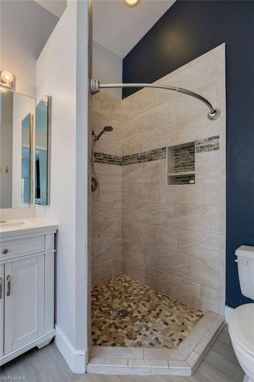 Walk-in shower with natural pebble flooring, large format wall tiling, and an accent mosaic tile band