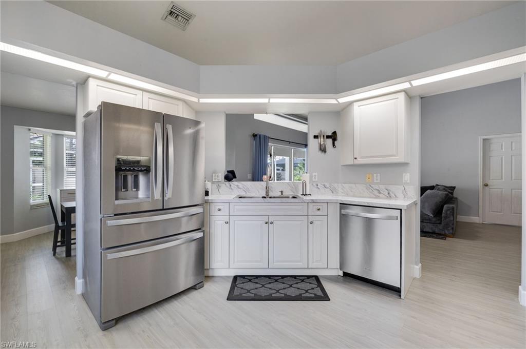 Modern kitchen featuring white cabinetry, stainless steel appliances, marble-look countertops, and wood-finish flooring