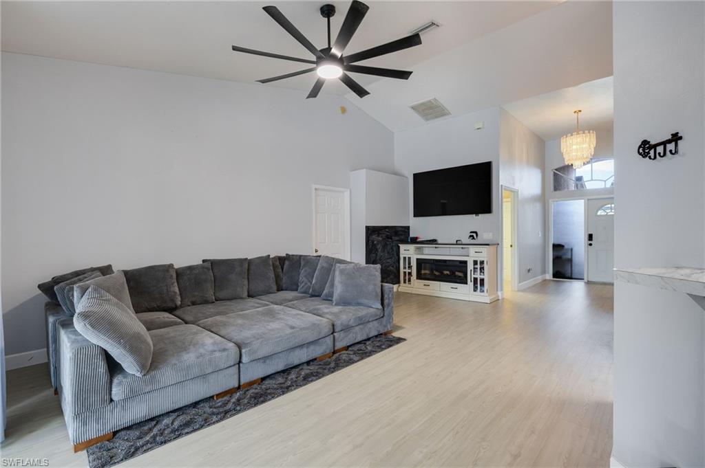 Spacious living area featuring light wood-finish flooring, vaulted ceilings, and a contemporary ceiling fan
