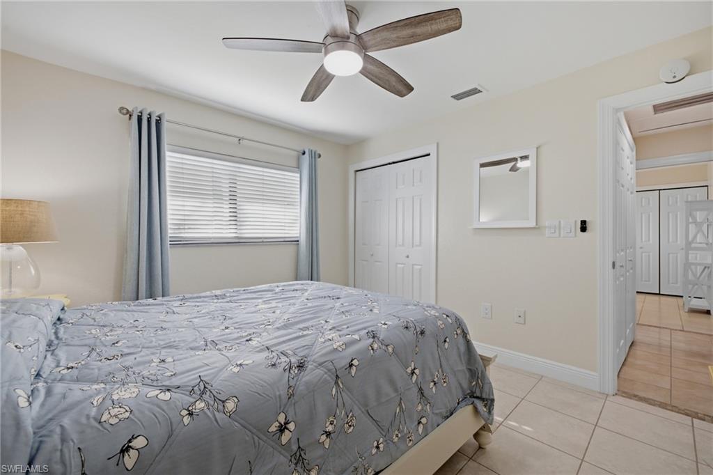Bedroom featuring tile flooring, a window with horizontal blinds, a ceiling fan with light fixture, and bifold closet doors
