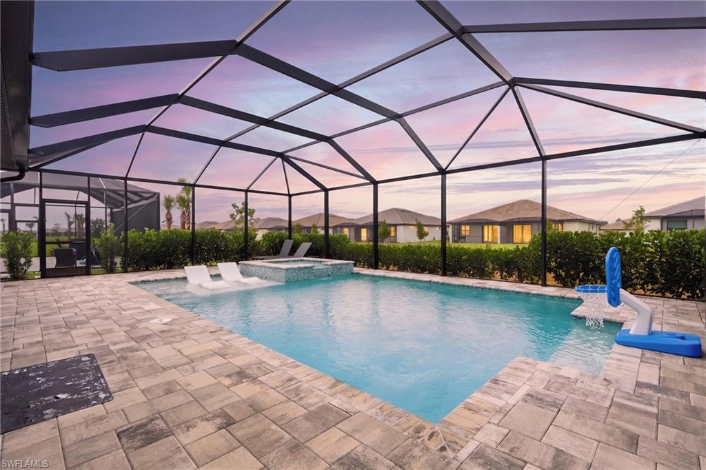 Screened-in outdoor living space featuring a swimming pool, integrated spa, and extensive paver decking