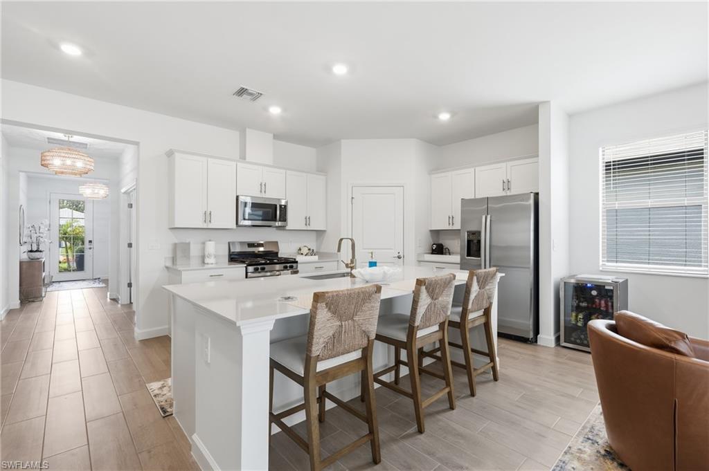 Modern kitchen featuring a large central island with seating, white shaker cabinetry, stainless steel appliances, and sleek countertops