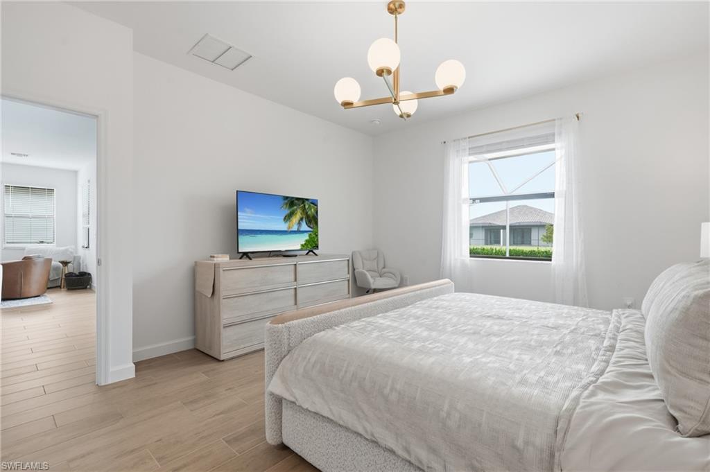 Bright interior space featuring light wood-finish flooring, a contemporary ceiling light fixture, and a large window with sheer drapery