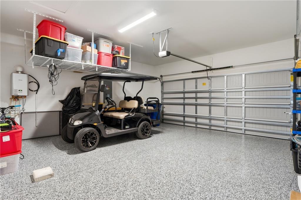 Garage interior featuring an epoxy flake floor coating, overhead storage racks, a tankless water heater, a sectional garage door, and built-in shelving
