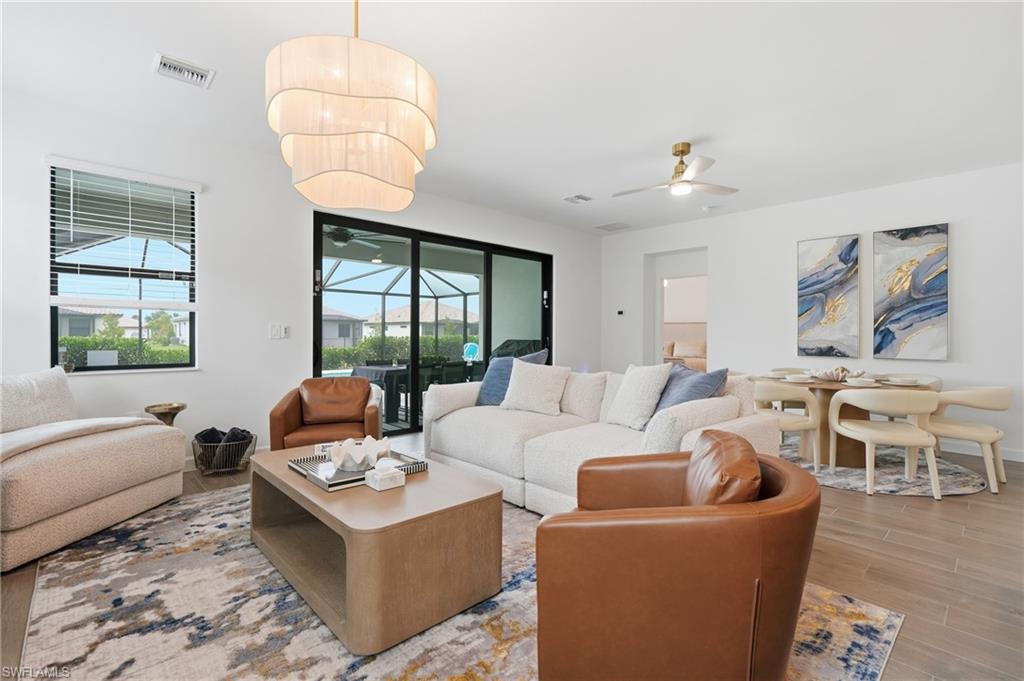 Open-concept living space featuring wood-finish flooring, a contemporary tiered chandelier, and direct access to the screened patio through sliding glass doors