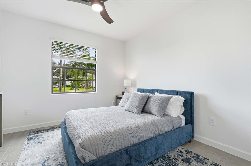 Bedroom featuring a ceiling fan with integrated lighting, a window with horizontal blinds, and wood-finish flooring