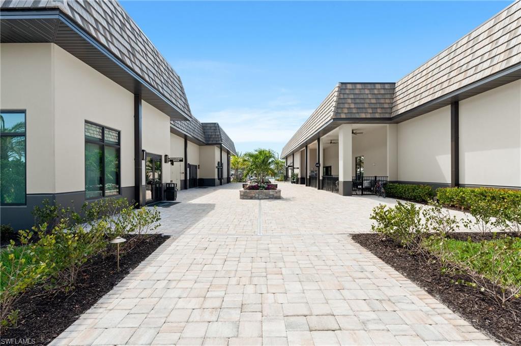Paved walkway bordered by manicured shrubs, leading between two structures with pitched, shingle-style roofs