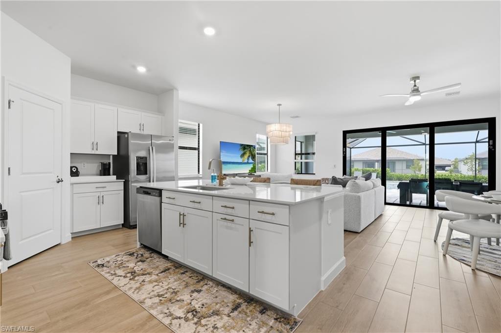 Open-concept living space featuring a central kitchen island with a white countertop, modern white cabinetry, and stainless steel appliances