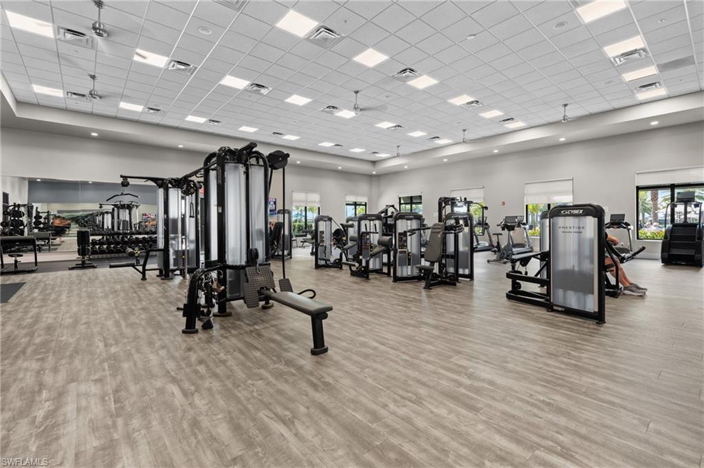 Expansive fitness center featuring wood-finish flooring, recessed lighting, ceiling fans, large windows with roller shades, and a comprehensive selection of exercise equipment