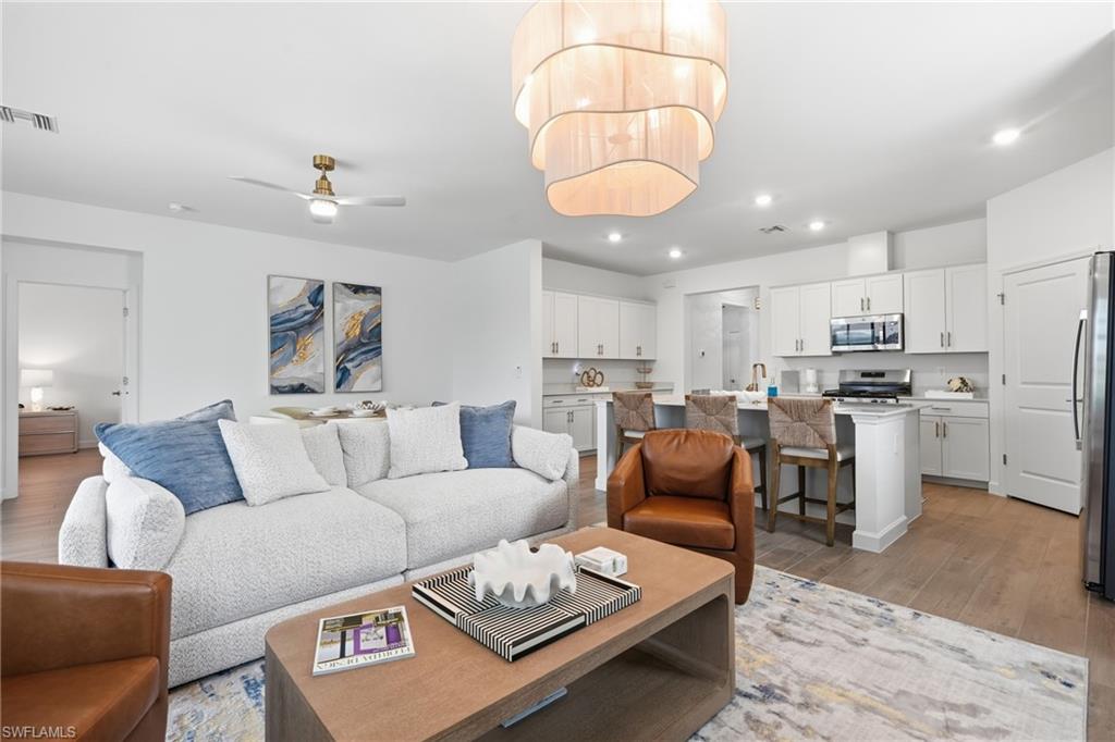 Open-concept living space featuring wood-finish flooring, a contemporary chandelier, recessed lighting, and a kitchen with white cabinetry and stainless steel appliances
