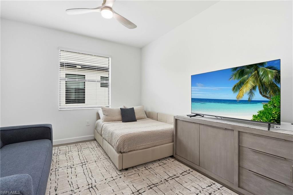 Light-filled interior space featuring a window with white blinds, a ceiling fan, and a light-toned wood-finish media console