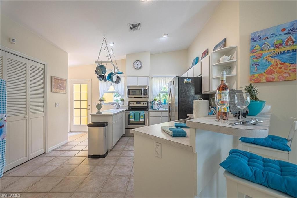 Kitchen with stainless steel appliances, light countertops, a peninsula, open shelves, and light tile patterned flooring