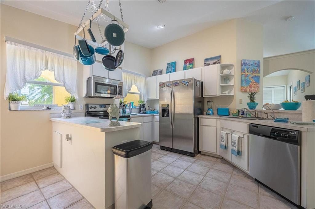 Kitchen featuring appliances with stainless steel finishes, a peninsula, light countertops, arched walkways, and open shelves