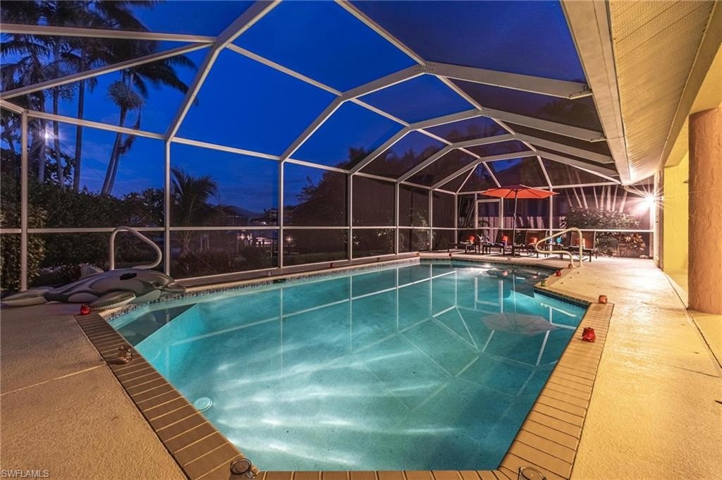Pool at night with an outdoor pool, a patio area, and glass enclosure