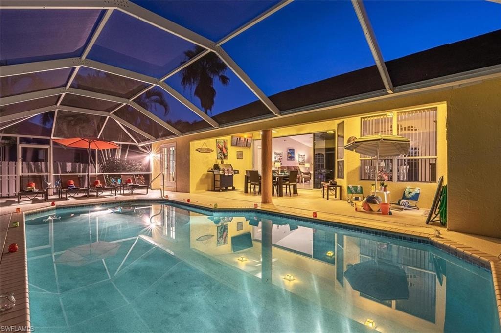 Pool at night featuring an outdoor pool, a patio, and glass enclosure