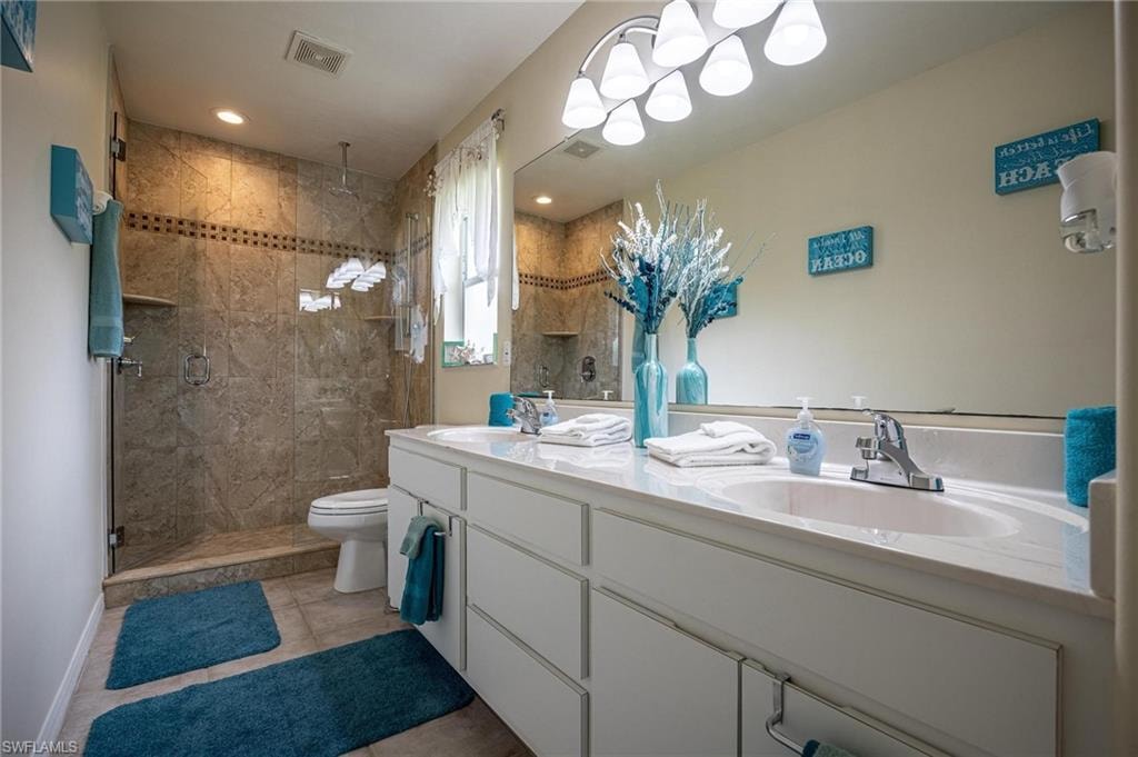 Bathroom with double vanity, a stall shower, toilet, tile patterned floors, and baseboards