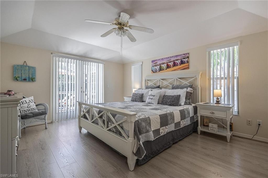 Bedroom featuring a raised ceiling, wood finished floors, a ceiling fan, access to exterior, and baseboards