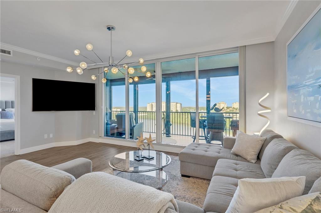 Living area with wood finished floors, ornamental molding, suspended lighting, and expansive windows