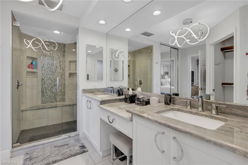 Bathroom with double vanity, a stall shower, hanging lights, and a walk in closet