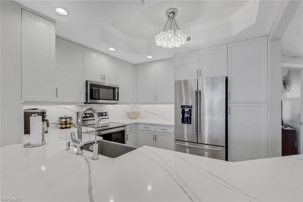 Kitchen featuring stainless steel appliances, ornamental molding, light stone countertops, white cabinetry, and hanging light fixtures