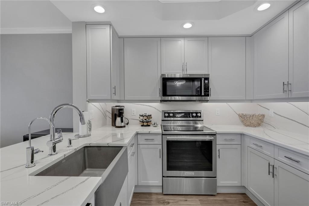 Kitchen with stainless steel appliances, light stone counters, recessed lighting, crown molding, and light wood-style flooring