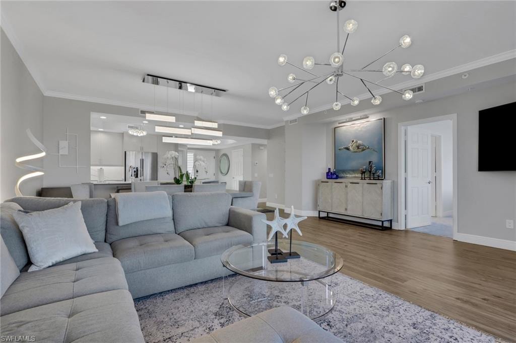 Living room with ornamental molding, wood finished floors, and hanging lights