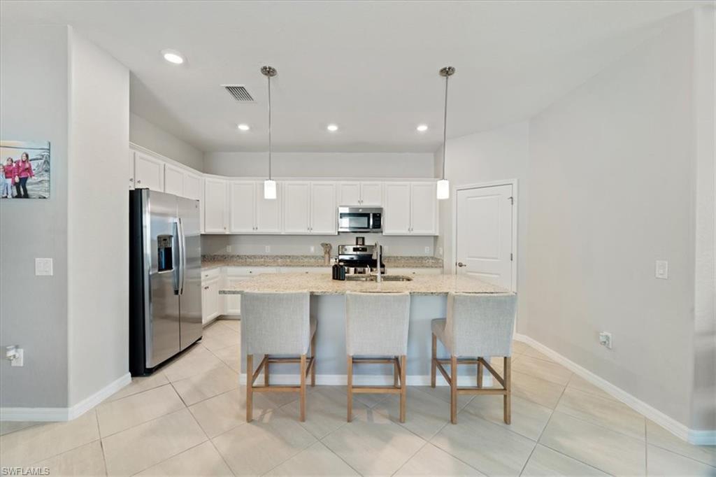 Kitchen featuring a central island with integrated sink, white cabinetry, stainless steel appliances, granite countertops, and tile flooring