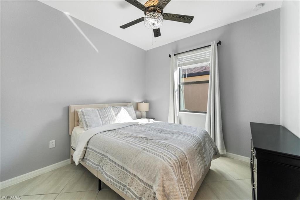 Light gray interior walls with a single window, a dark wood-finish ceiling fan with a decorative light fixture, and light-toned tile flooring