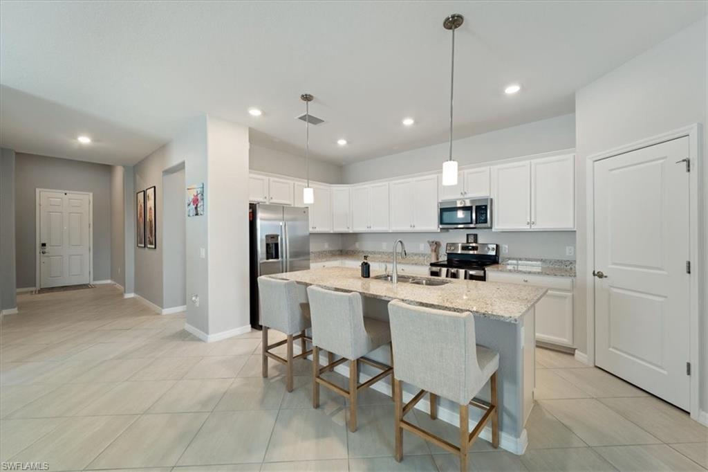 Contemporary kitchen featuring white cabinetry, light-colored countertops, a large center island with an integrated sink, and stainless steel appliances