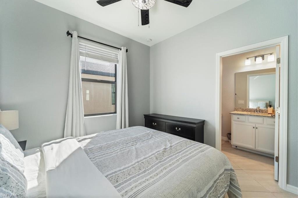Bedroom featuring a window with blinds and curtains, a ceiling fan with light fixture, and an entry to a bathroom
