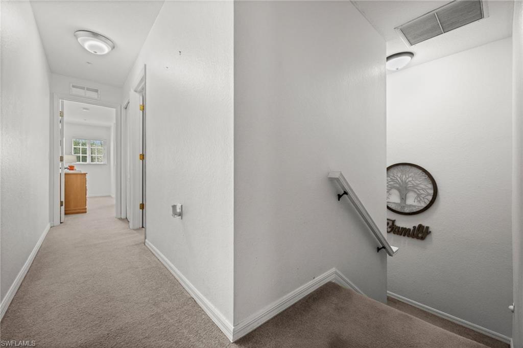 Carpeted hallway and staircase featuring light-colored walls, white trim, and flush-mount lighting fixtures
