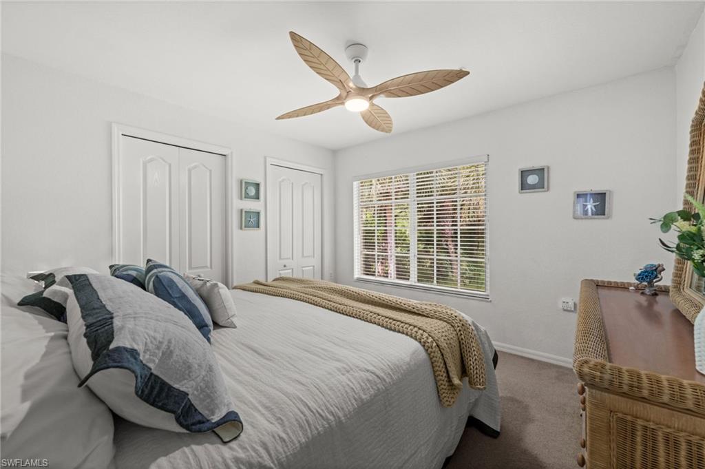 Bedroom featuring a ceiling fan, two white bi-fold closet doors, a window with horizontal blinds, and carpeting