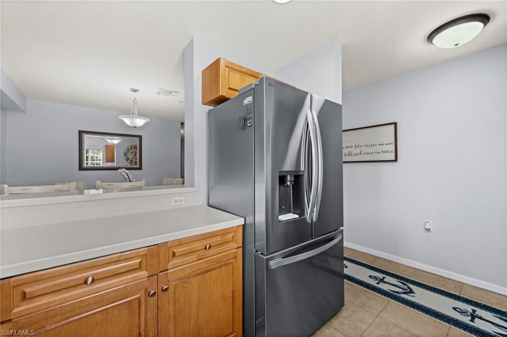Kitchen area featuring wood cabinetry, light-colored countertops, a stainless steel refrigerator, and tiled flooring
