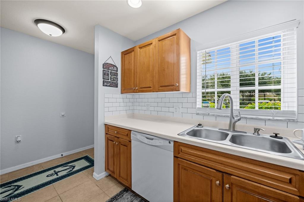 Kitchen featuring wood cabinetry, a double basin stainless steel sink with a modern faucet, white subway tile backsplash, and light-toned countertops