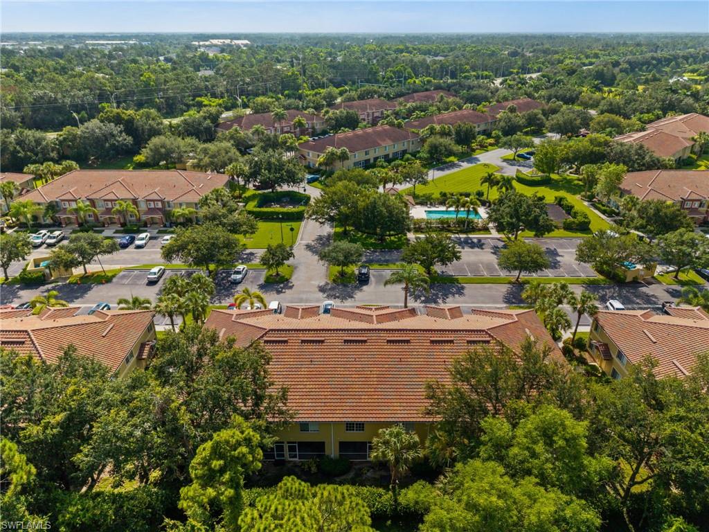Expansive community showcasing lush landscaping, multiple buildings with terra cotta tile roofs, and abundant mature trees