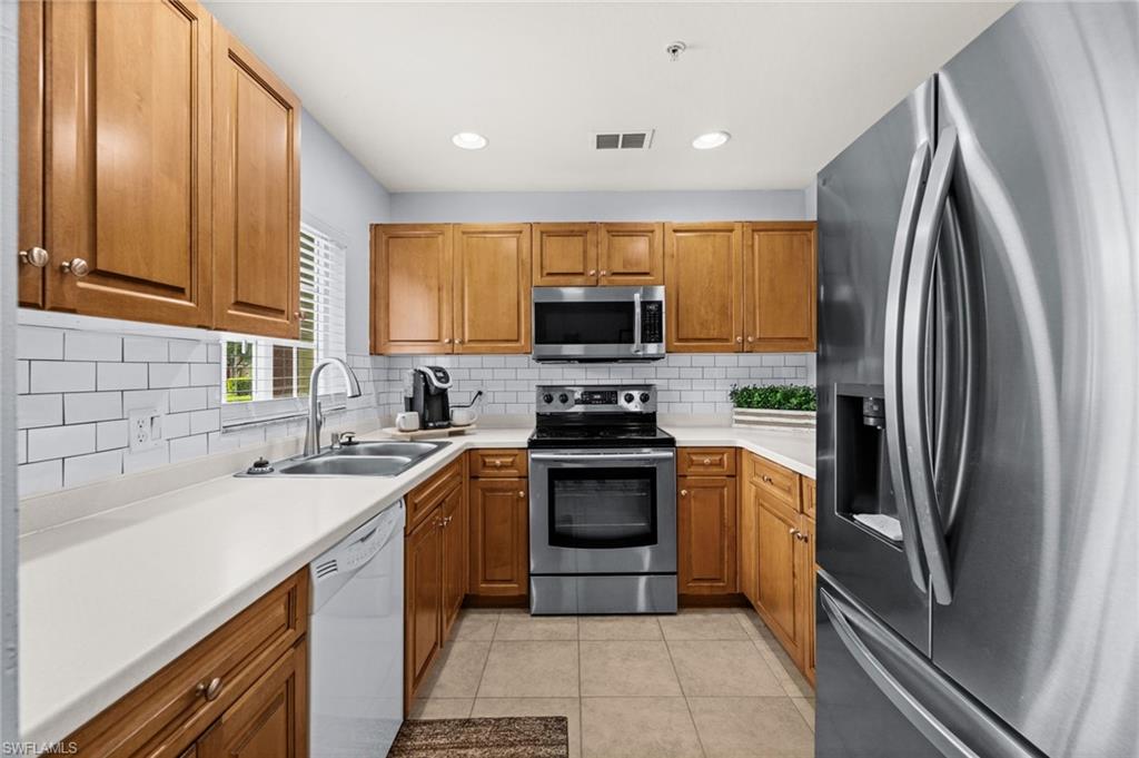 U-shaped kitchen featuring wood cabinetry, stainless steel appliances, white subway tile backsplash, and light-colored countertops