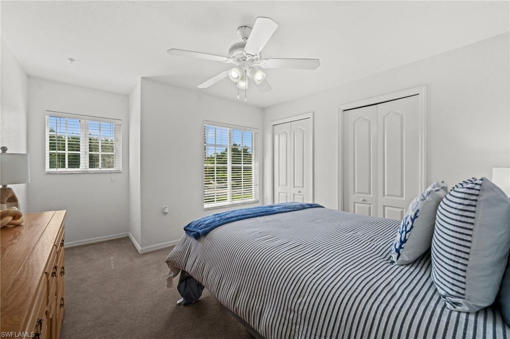 Carpeted bedroom featuring two windows with horizontal blinds, a white ceiling fan, and two bifold closet doors