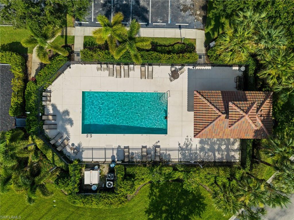 Rectangular swimming pool with a surrounding paved deck, enclosed by a fence and lush landscaping