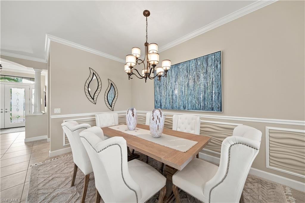 Dining area featuring a chandelier, decorative wall paneling, crown molding, and tiled flooring extending into an entry hall with double glass doors