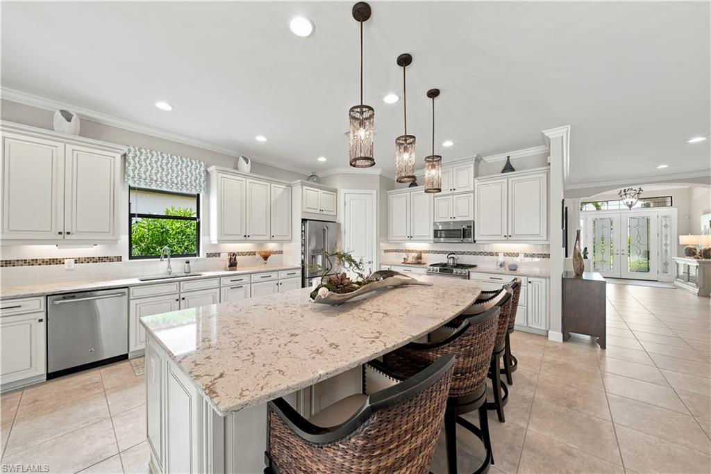 Open-concept kitchen featuring an expansive island with seating, white shaker cabinetry, stainless steel appliances, pendant lighting, and tile flooring