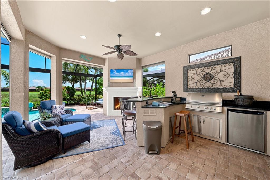 Expansive outdoor living area featuring a built-in outdoor kitchen with grill and refrigerator, a ceiling fan, a fireplace, and a large screened enclosure overlooking a pool