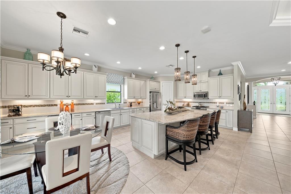 Open-concept kitchen and dining area featuring white shaker-style cabinetry, a large kitchen island with pendant lighting, stainless steel appliances, and tile flooring