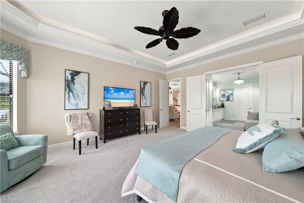Carpeted bedroom featuring a tray ceiling with crown molding, a decorative ceiling fan, and light-toned wall paint