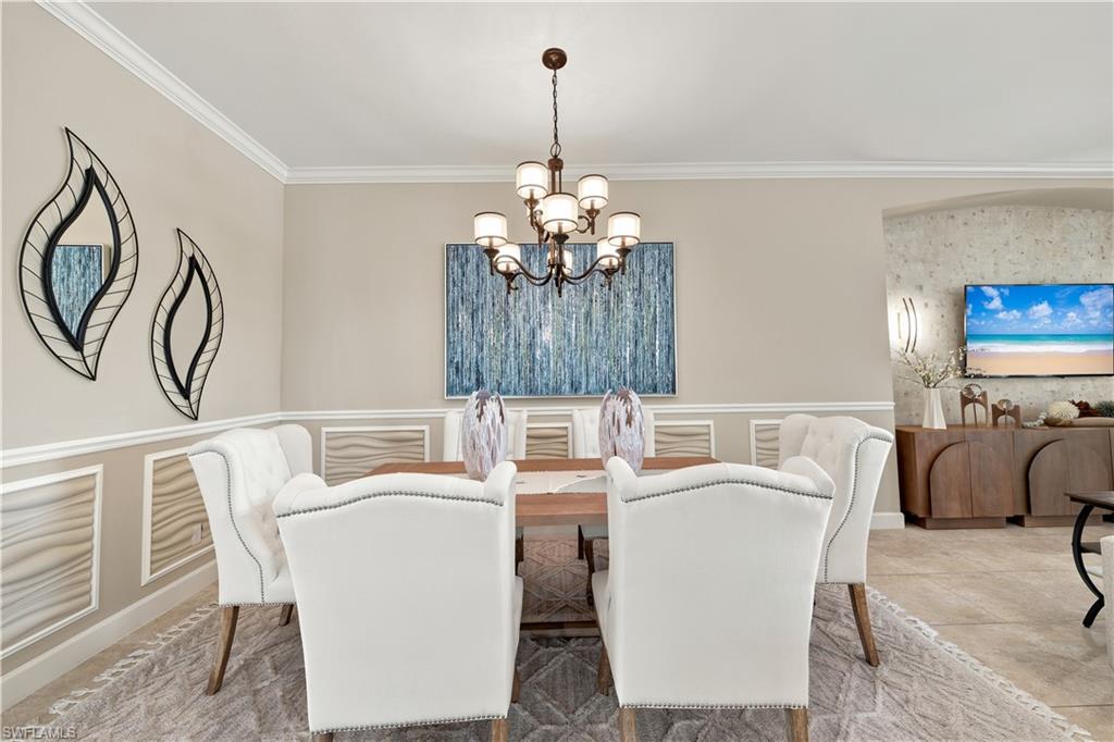 Dining area featuring crown molding, a multi-arm chandelier, and wainscoting details with textured panels