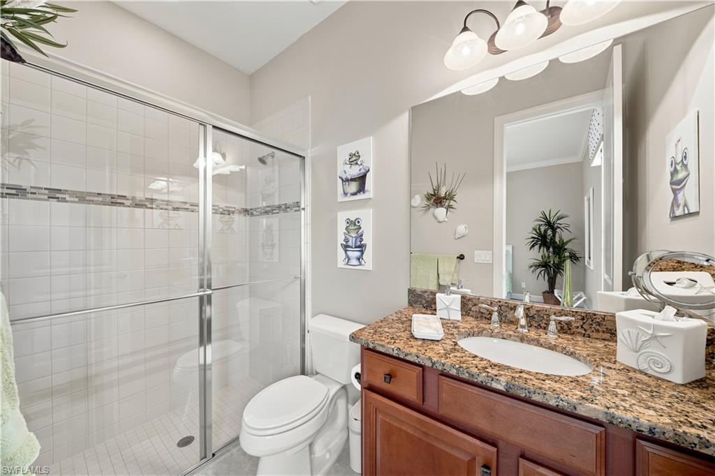 Bathroom featuring a walk-in shower with clear glass enclosure and decorative tile accent band, a single vanity with stone countertop and undermount sink, and a commode